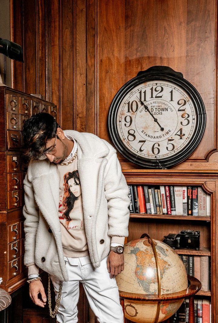Fam Mirza beside a large clock in a wood-paneled study.